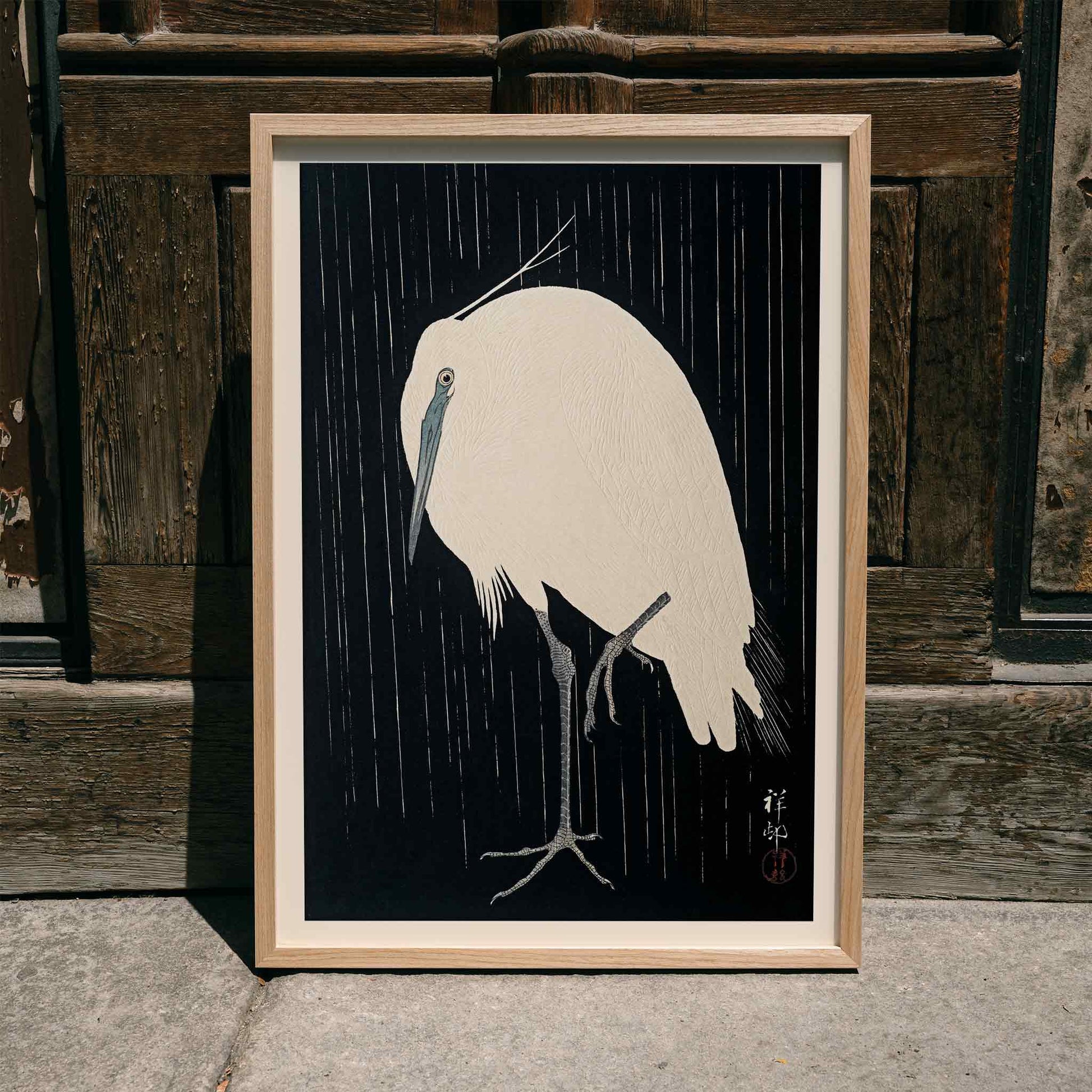 White egret standing in the rain art print poster with dark background by Ohara Koson, framed and displayed in modern living room decor